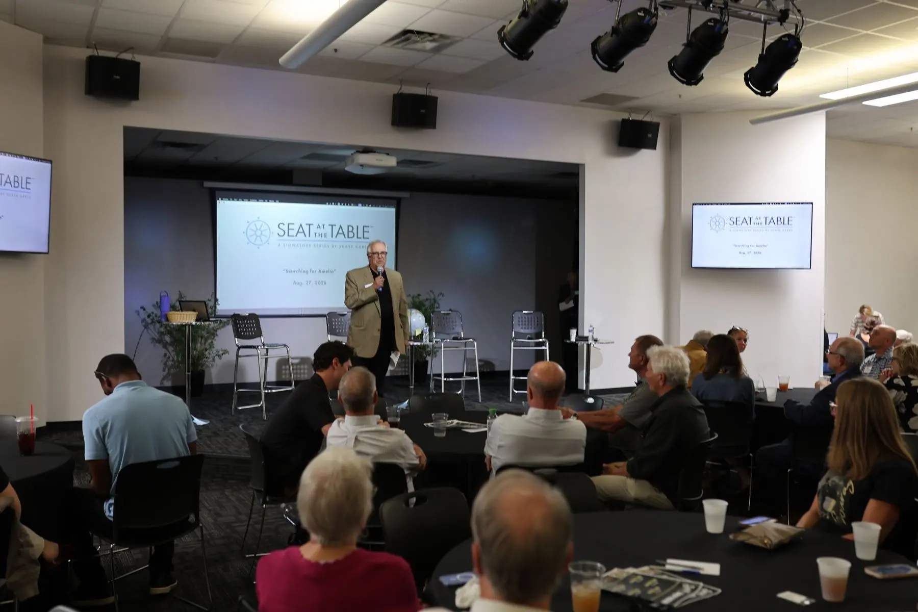 Remarks from the front of the room, the Seat at the Table title on screen behind